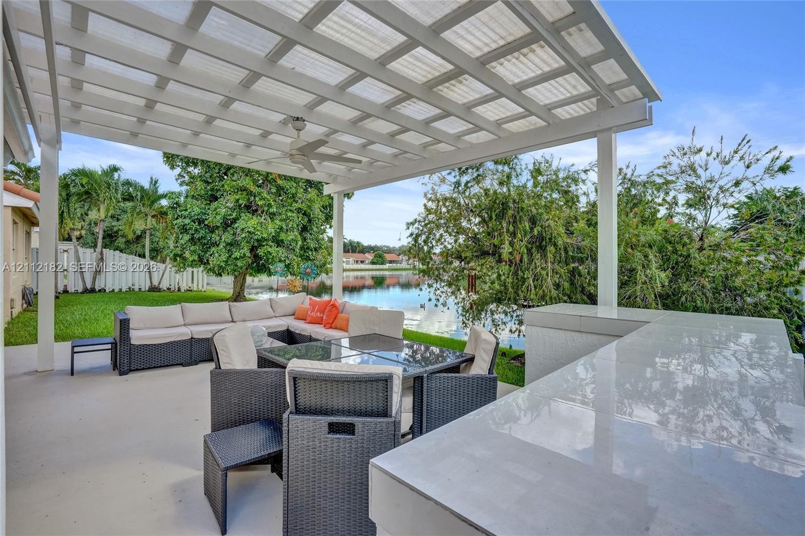 Covered patio featuring a white pergola, built-in stone countertop, ceiling fan, and concrete flooring