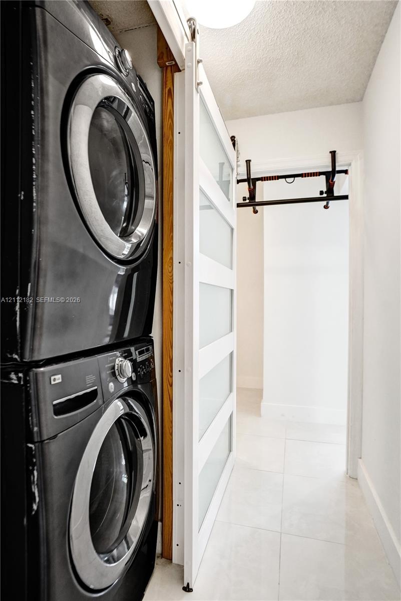 Stacked laundry units featuring a white sliding door with frosted glass panels and large-format tile flooring