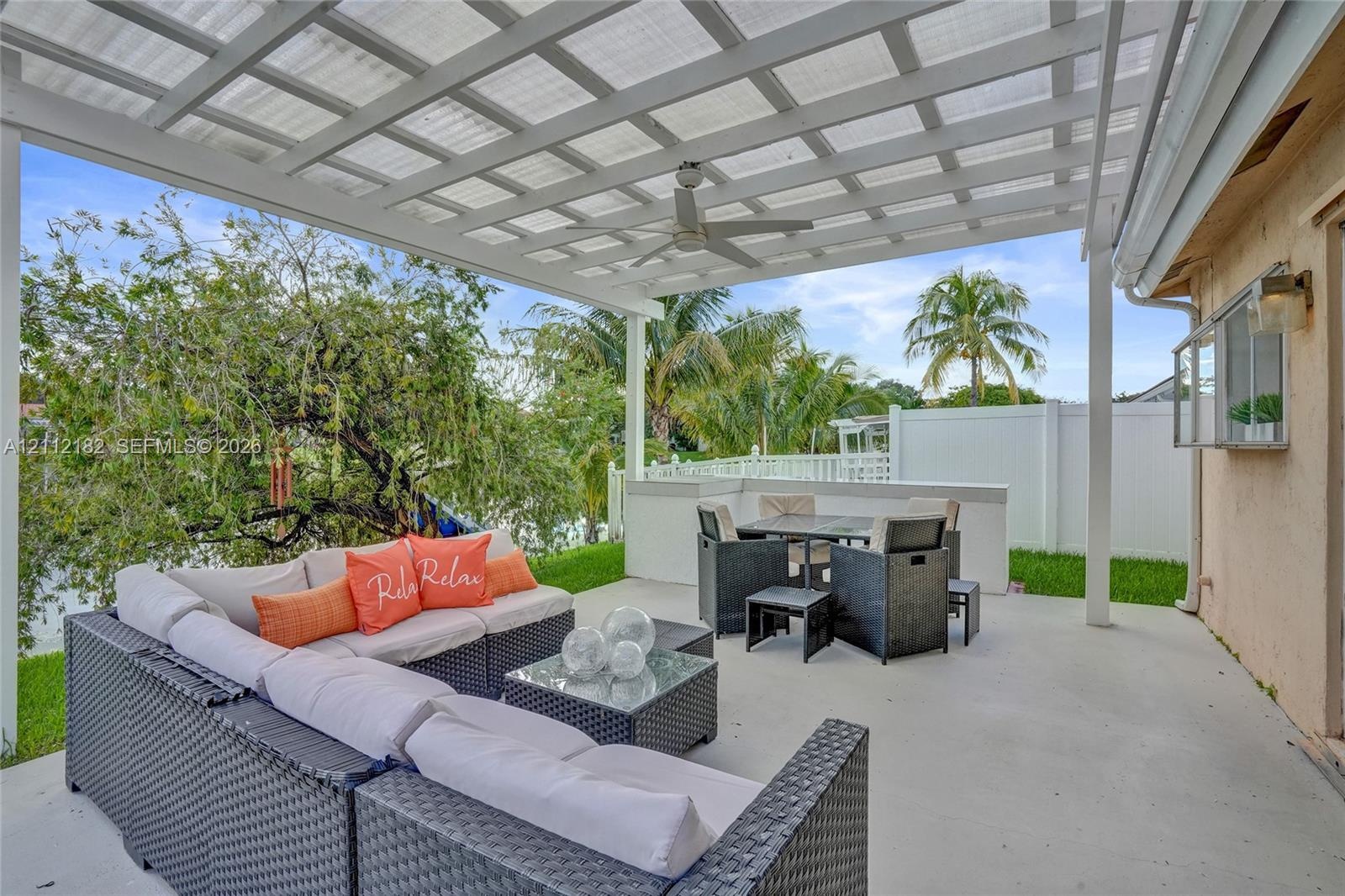 Covered patio featuring a white pergola, ceiling fan, concrete flooring, and solid white fencing
