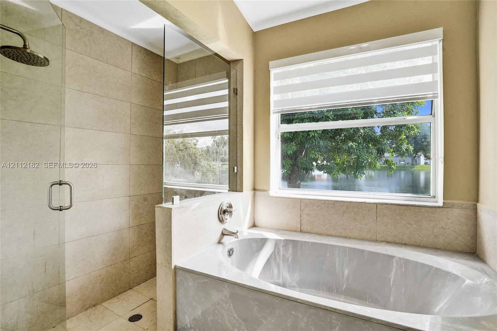 Walk-in shower with floor-to-ceiling tile, soaking tub with surround tiling, frameless glass enclosure, and a window providing water exposure