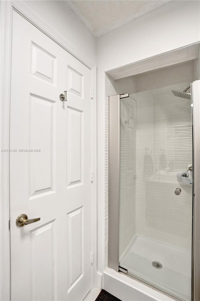 Walk-in shower featuring a glass door, textured wall tile, a rainfall showerhead, and a satin-finish lever handle