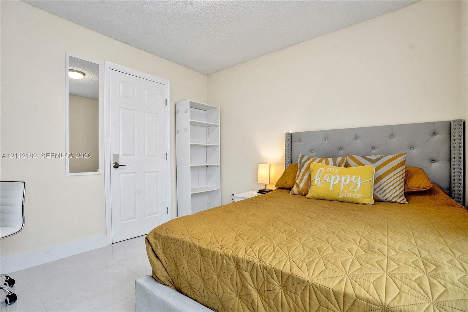 Room featuring neutral wall paint, white tile flooring, a wall-recessed mirror, and a built-in floor-to-ceiling white shelving unit
