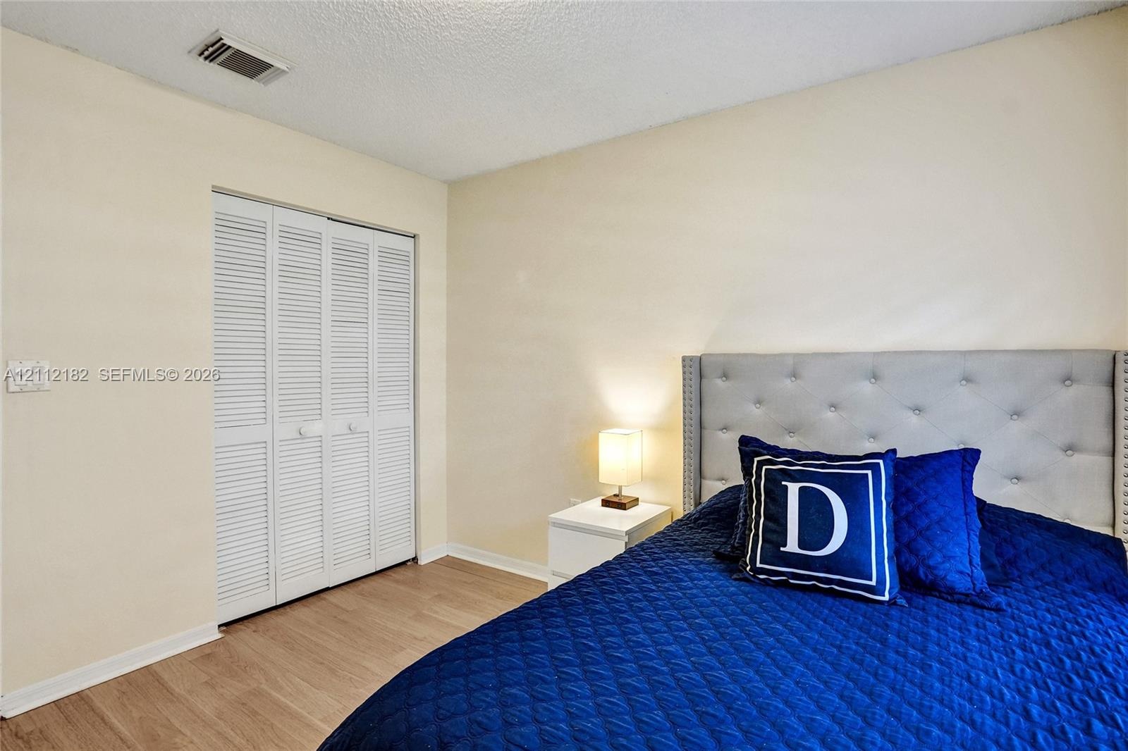 Neutral-toned walls, wood-finish flooring, and a closet with white louvered bifold doors