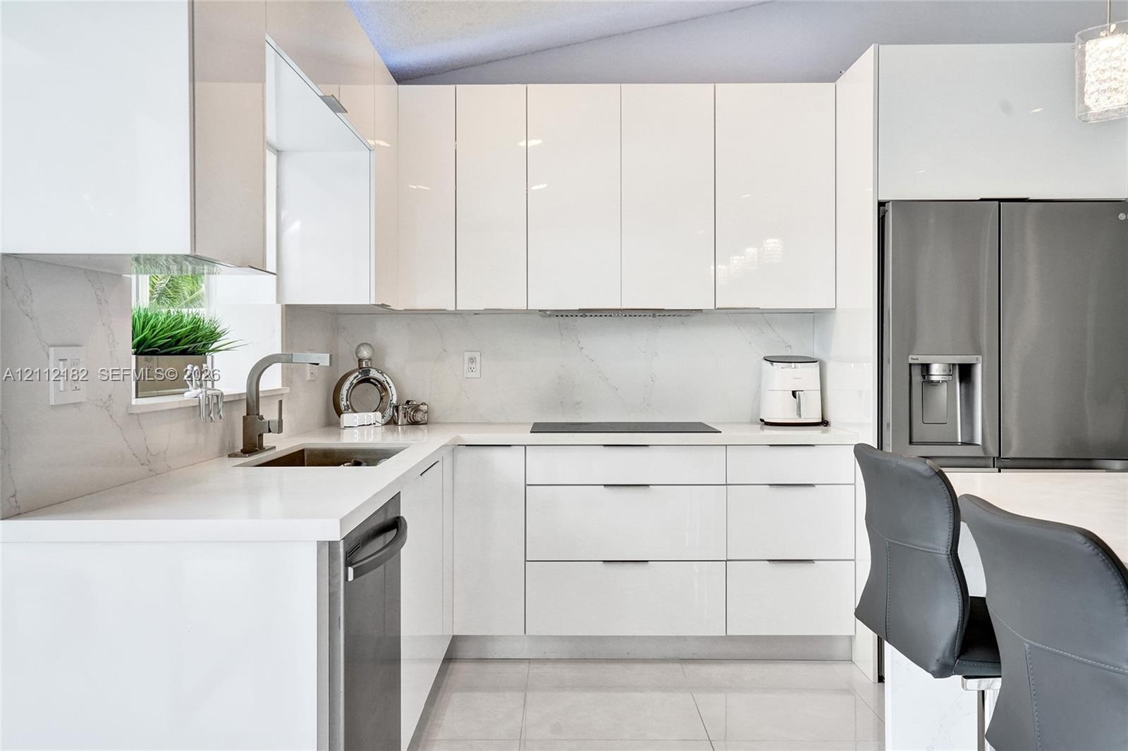 Modern kitchen featuring high-gloss cabinetry, stone-finish countertops, full-height backsplash, undermount sink with a gooseneck faucet, and integrat