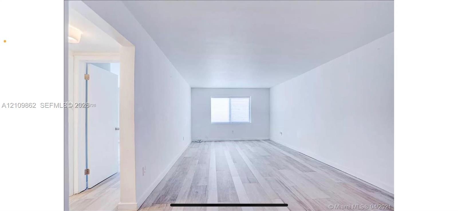 Neutral interior space featuring wood-finish flooring, a rectangular window, and a white door with a metal handle