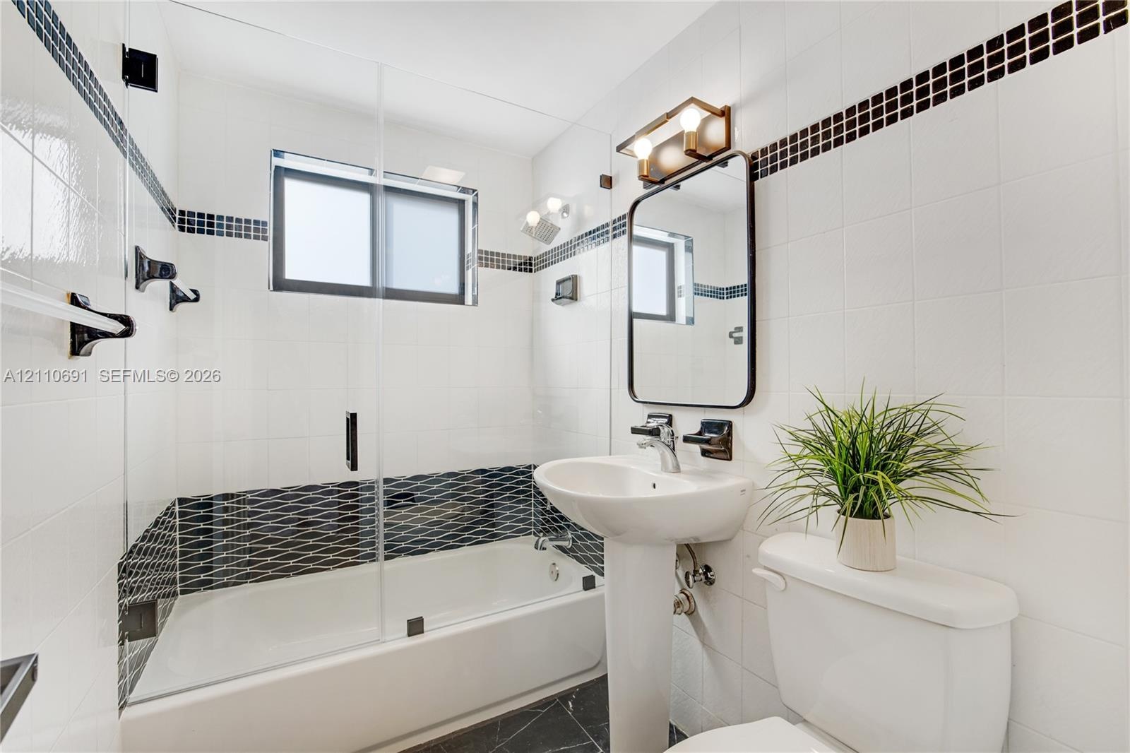 Bathroom featuring a pedestal sink, a glass-enclosed shower-tub combination, and black-and-white tile accents throughout
