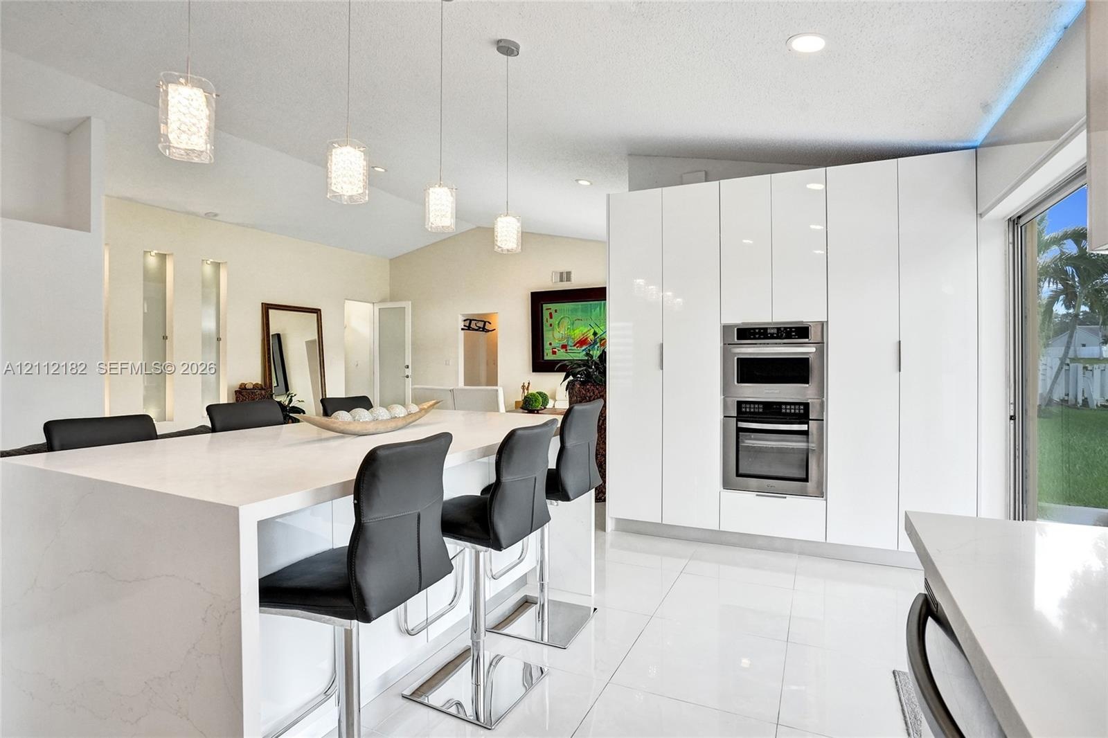 Modern kitchen featuring white flat-panel cabinetry, a central island with a solid surface countertop, built-in stainless steel double ovens, tile flo