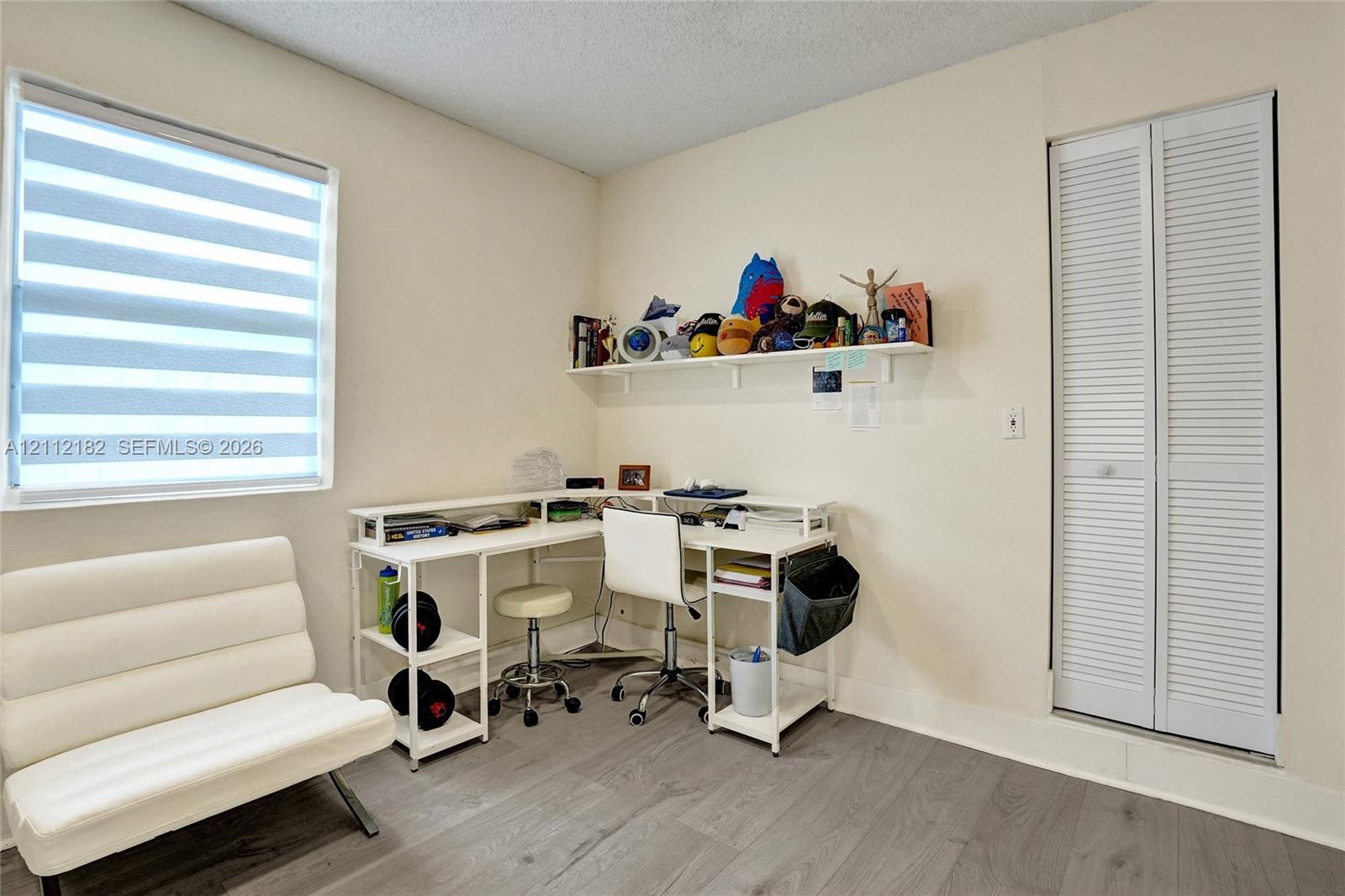 Wood-finish flooring, dual-pane window with zebra-style roller shades, and white louvered-style closet doors
