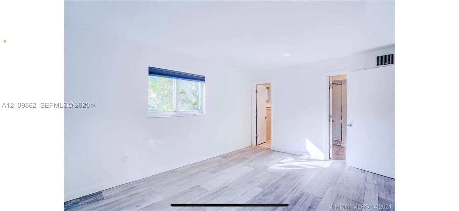 Neutral-toned interior room featuring wood-finish flooring, a single-pane sliding window, and solid core interior doors