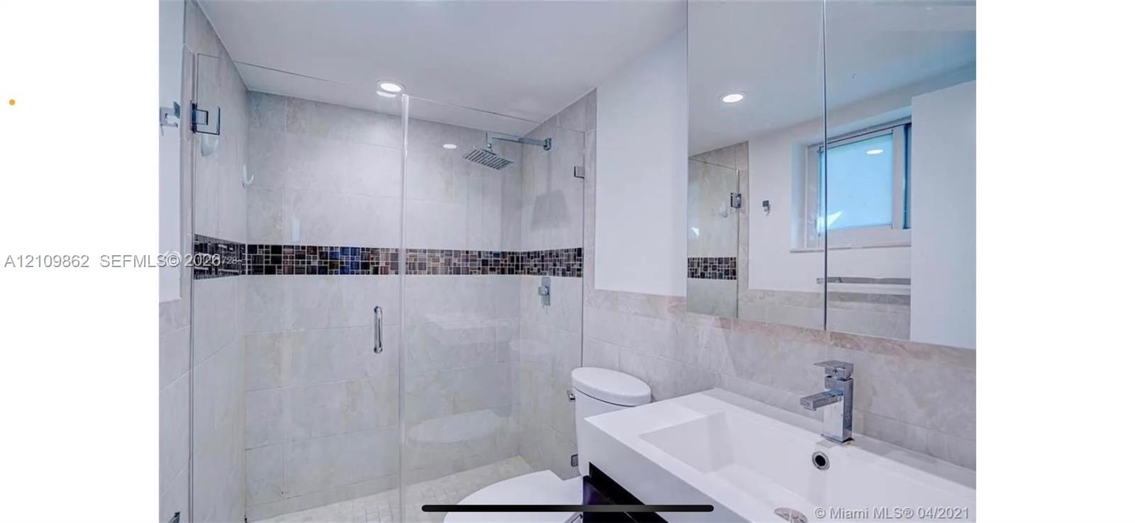 Modern bathroom featuring a glass-enclosed walk-in shower with stone tile walls, a decorative mosaic tile accent strip, a square rainfall showerhead, 