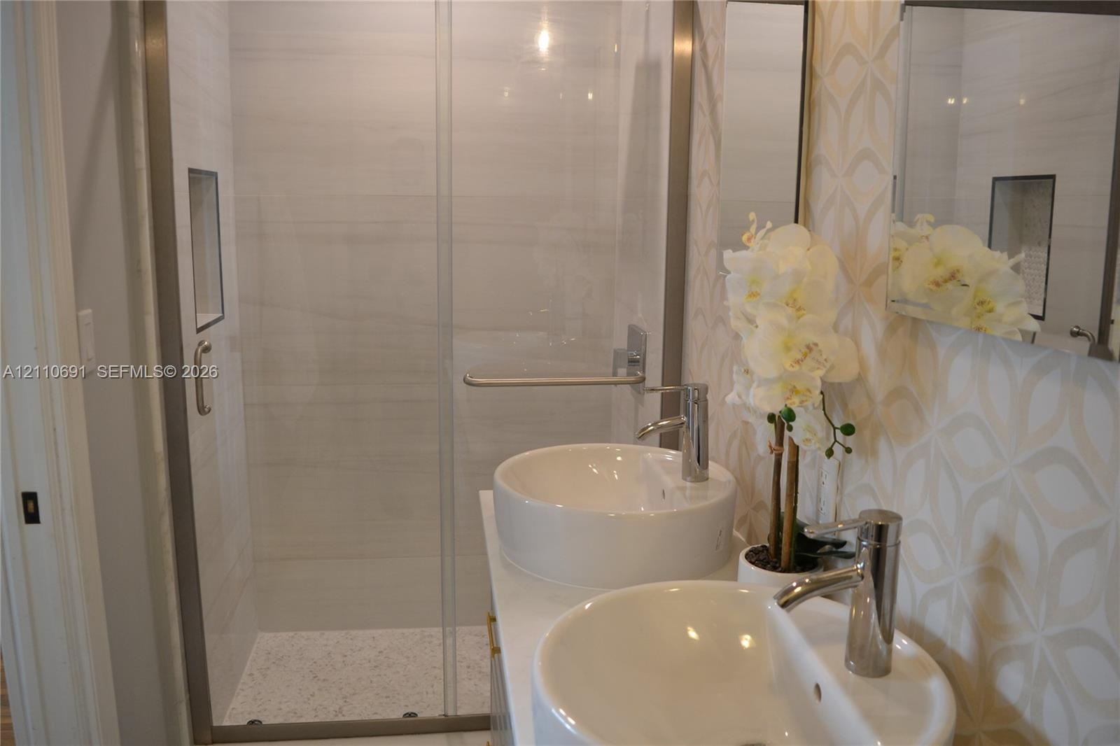 Walk-in shower with horizontal tile surround and integrated wall niche, featuring a dual-sink vanity with circular vessel sinks, polished chrome fauce