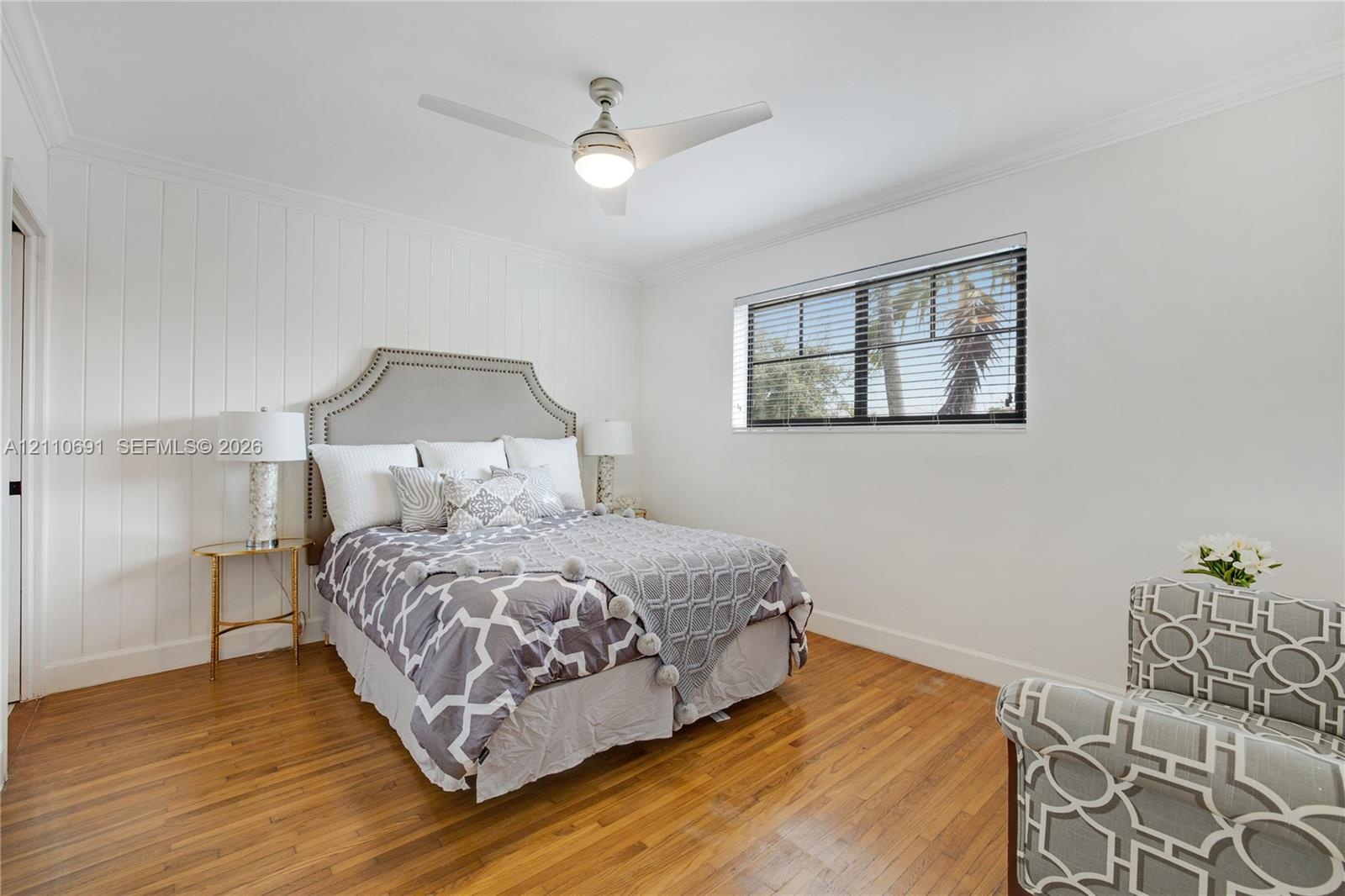 Room featuring wood-finish flooring, vertical plank wall detailing, crown molding, and a ceiling fan with integrated lighting