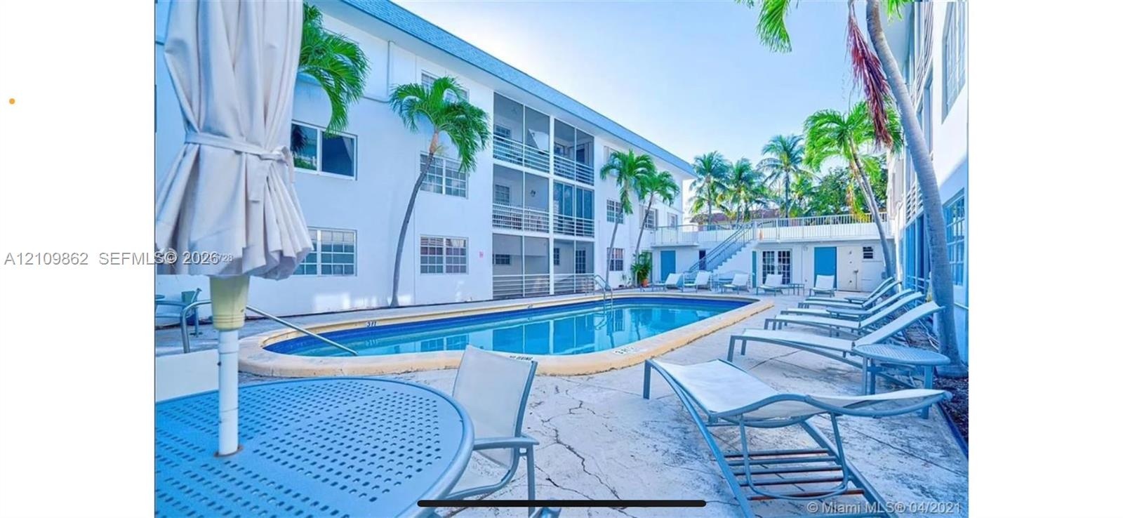 Outdoor community pool featuring a concrete deck, screen-enclosed balconies, and mature palm trees