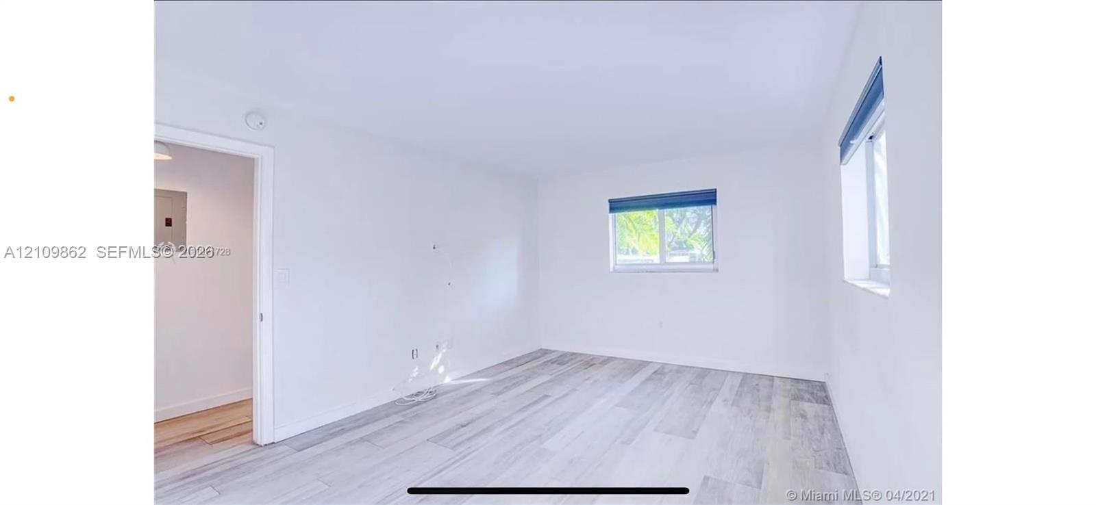 Neutral interior room featuring wood-finish flooring, white walls, and two windows