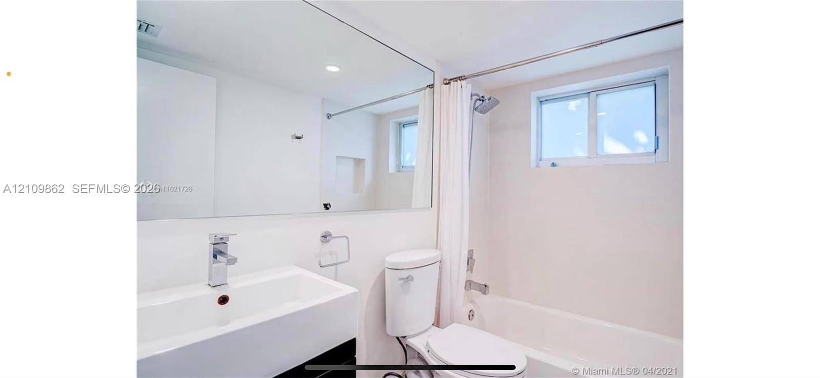 Bathroom featuring a rectangular vessel sink with a chrome faucet, large wall-mounted mirror, white elongated toilet, and a combination tub and shower