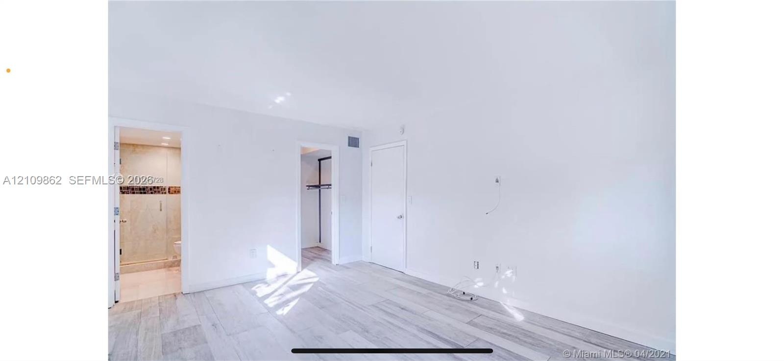 Interior space featuring neutral wall tones, light wood-finish flooring, a reach-in closet with built-in shelving, and a tiled bathroom with a glass-e