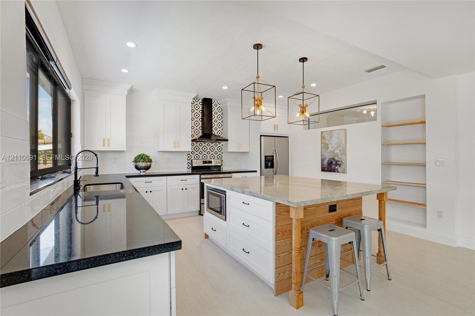 Kitchen featuring white shaker cabinetry, black stone countertops, geometric tile backsplash, central island with wood paneling, and open built-in she