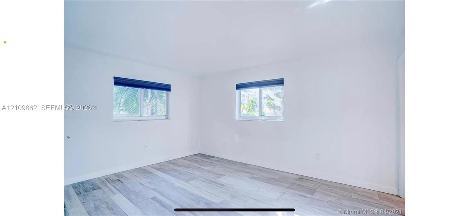Neutral interior space featuring wood-finish flooring, crisp white walls, and dual sliding windows