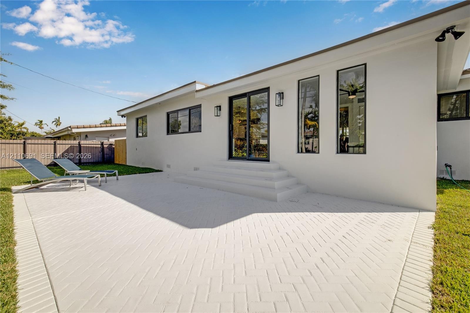 Rear exterior featuring a herringbone-patterned paved patio, white stucco siding, sliding glass doors, vertical rectangular windows, and exterior wall