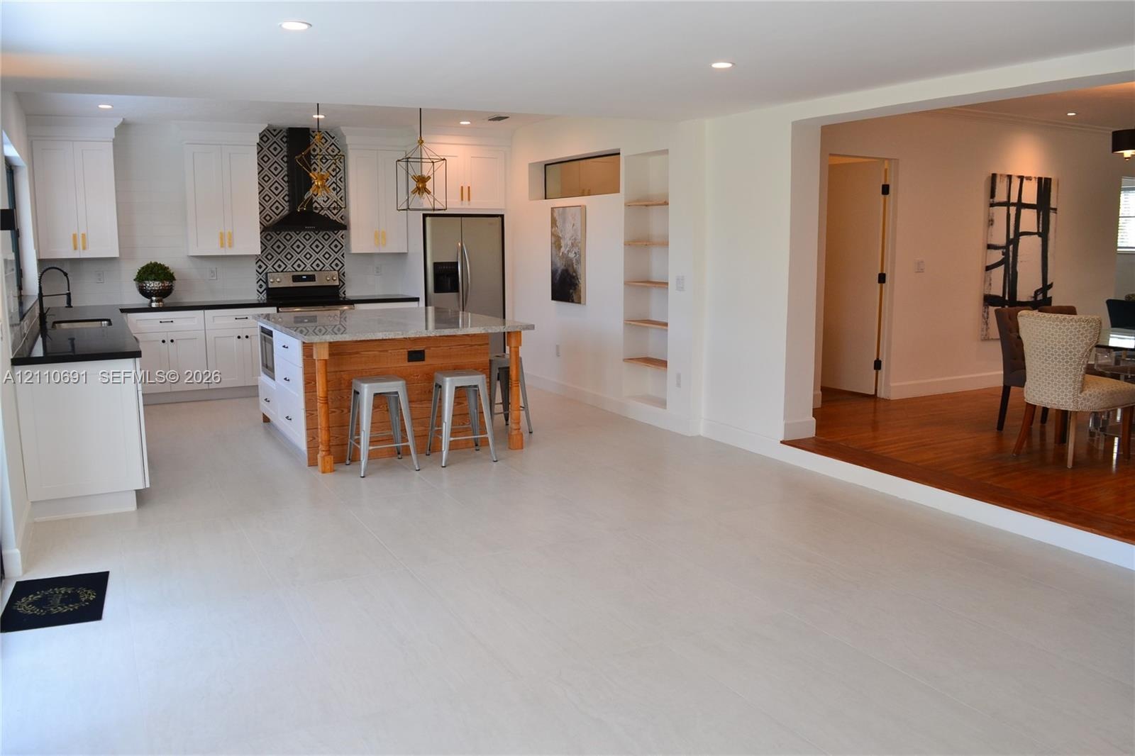 Kitchen featuring white shaker cabinetry, an island with a wood-finish base and stone countertop, geometric tile backsplash, stainless steel appliance