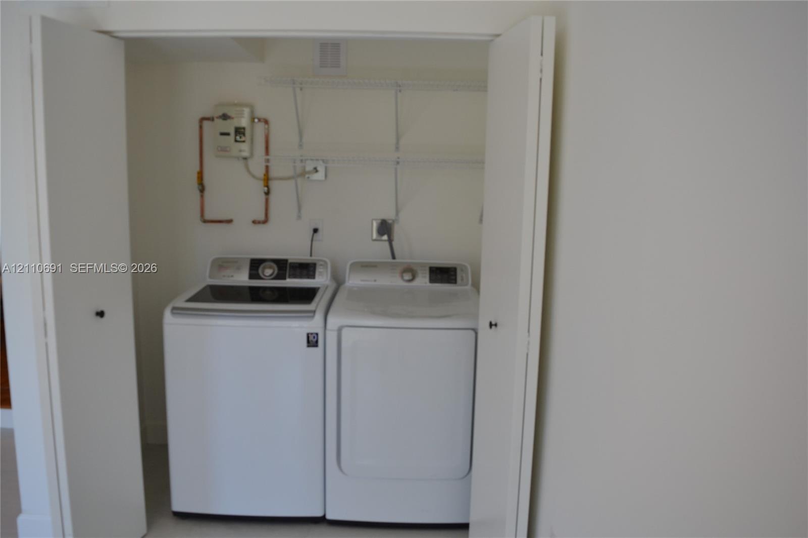 Laundry closet featuring white bifold doors, installed white washer and dryer, and wire shelving