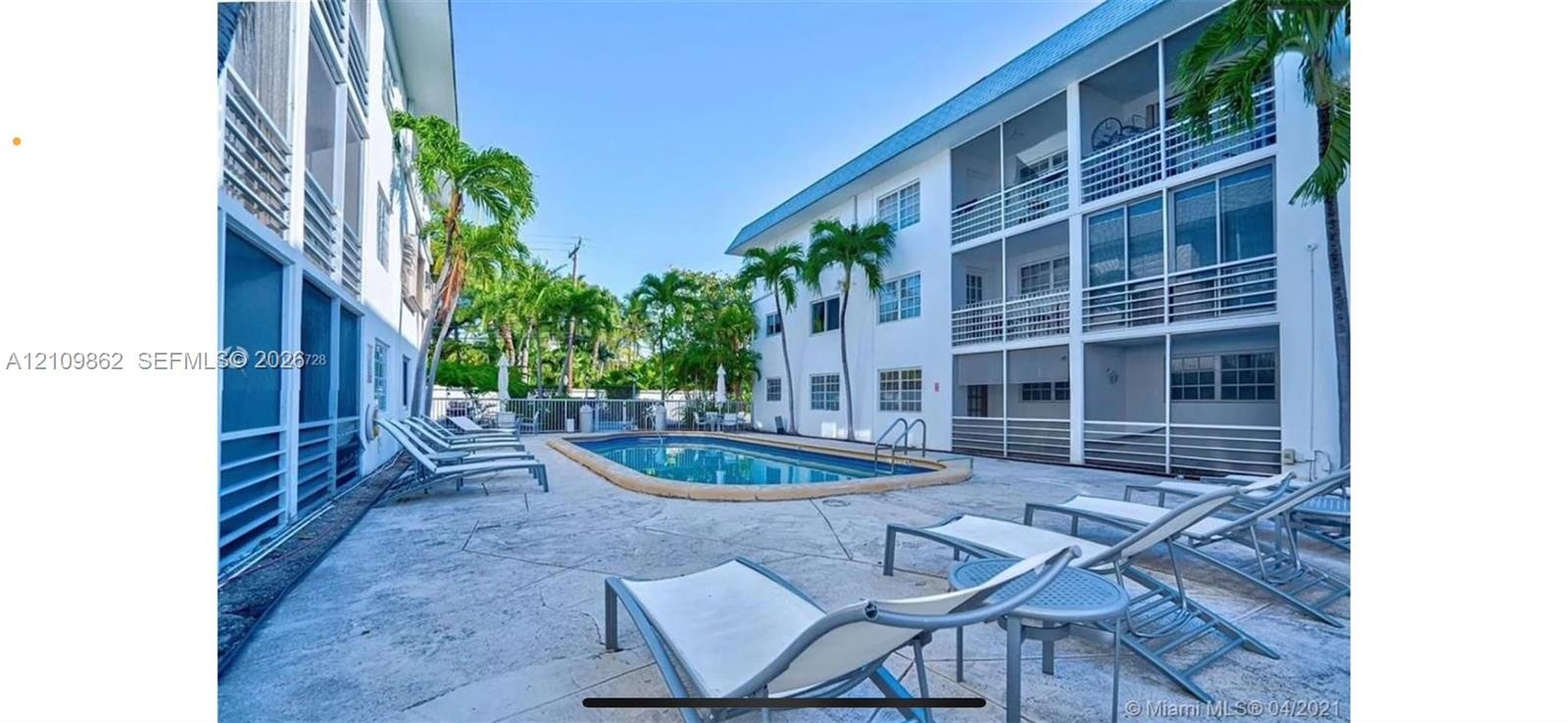 In-ground swimming pool with stone-style decking, multi-story structure with screened balconies, and mature palm trees