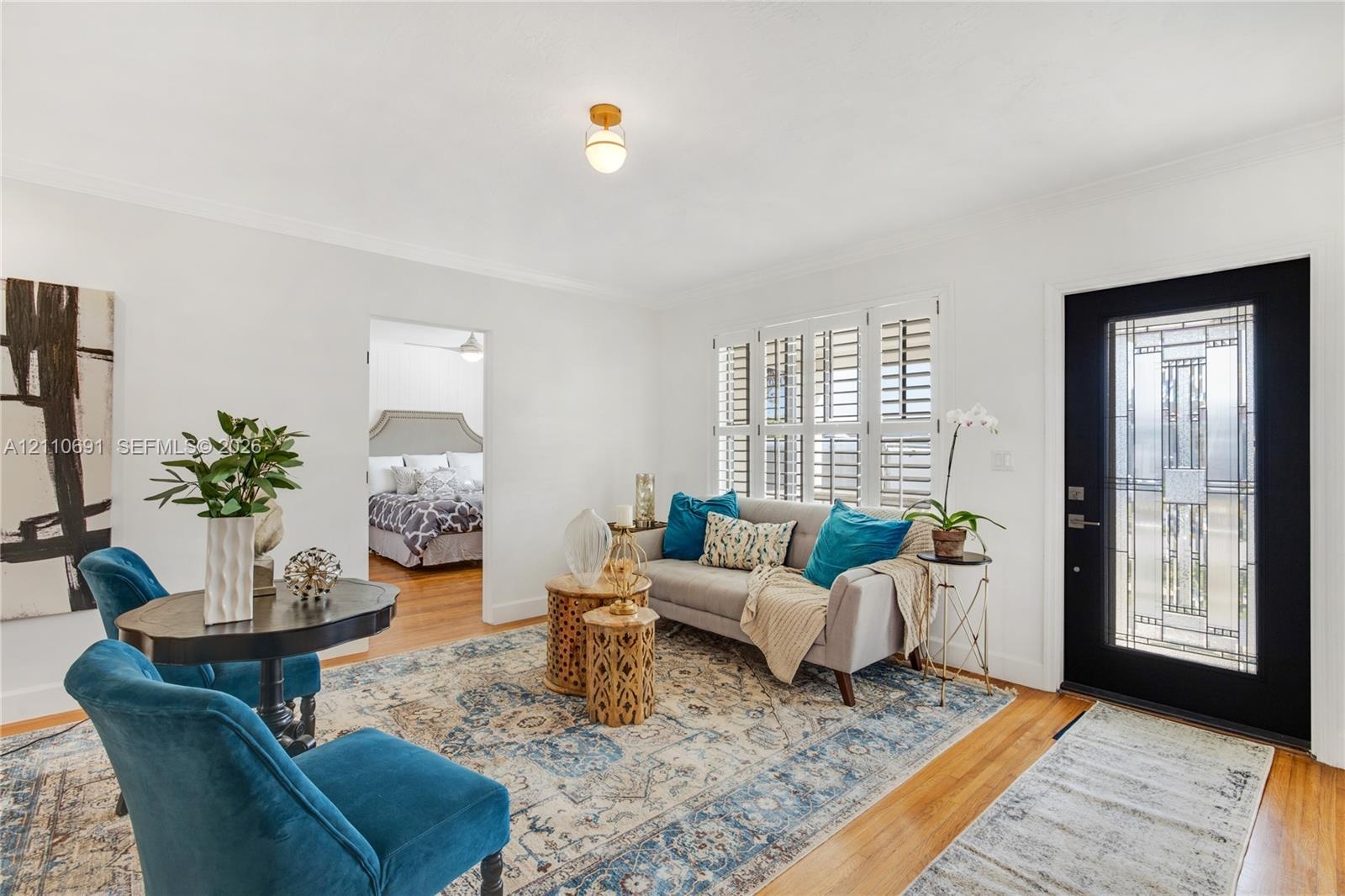 Wood-finish flooring, white walls, multi-pane casement windows with plantation shutters, globe-style ceiling lighting, and a black front door featurin