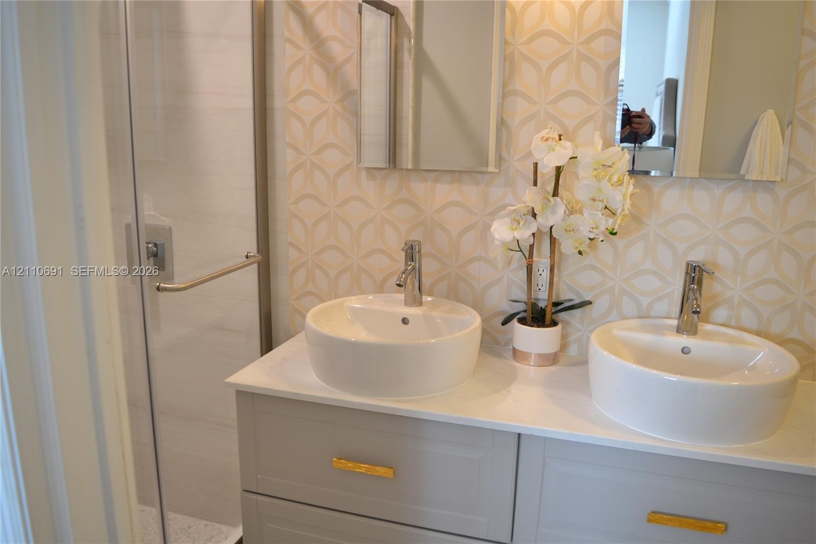 Double vanity featuring a stone-composite countertop, dual circular vessel sinks, gold-tone hardware, and a glass-enclosed shower