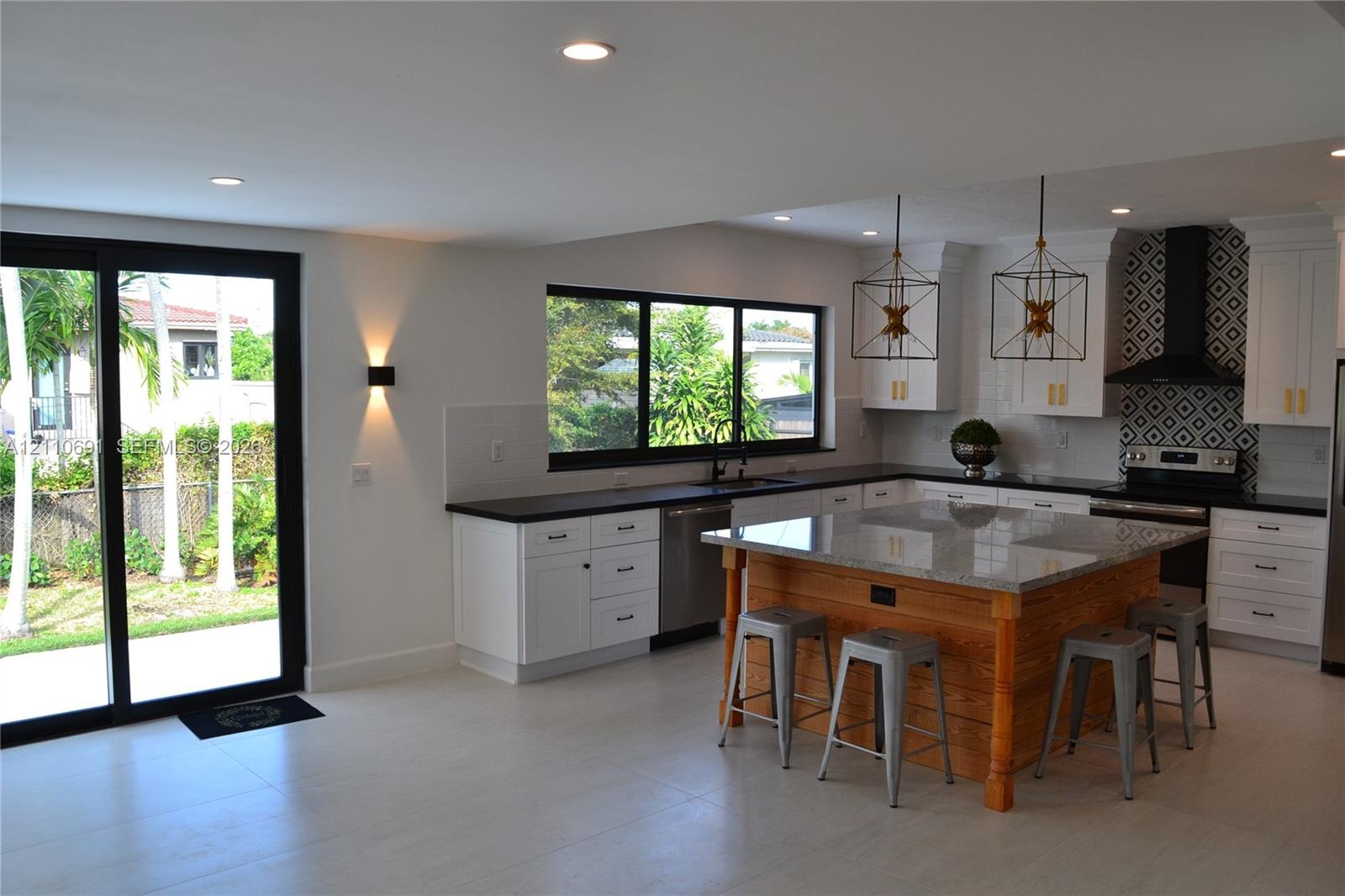 Kitchen featuring white cabinetry, a center island with wood-finish base and stone-surface countertop, geometric patterned tile backsplash, stainless 