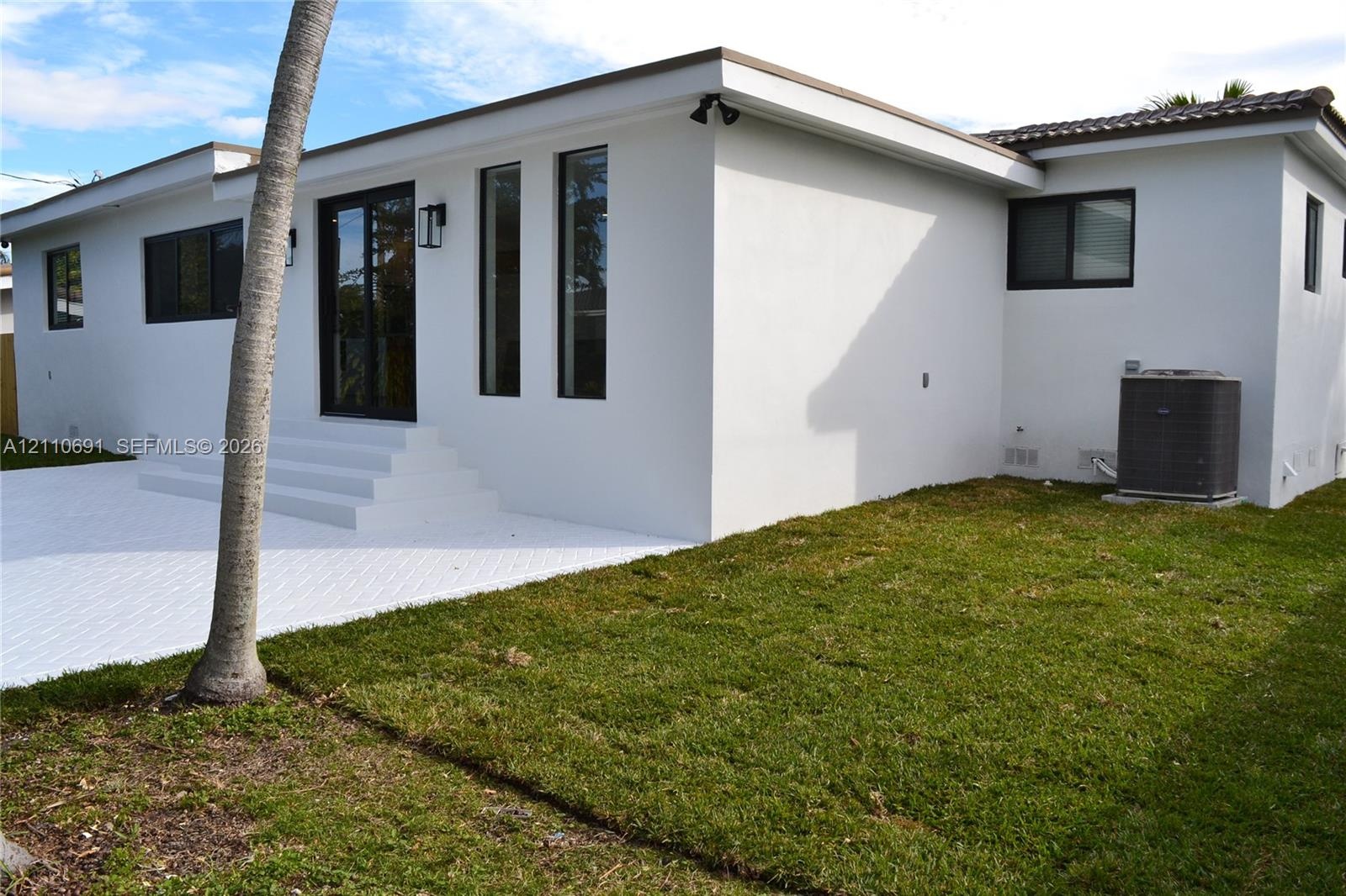 Stucco exterior featuring a white paved patio, tiered concrete steps, dark-framed glass doors, and dark-framed windows