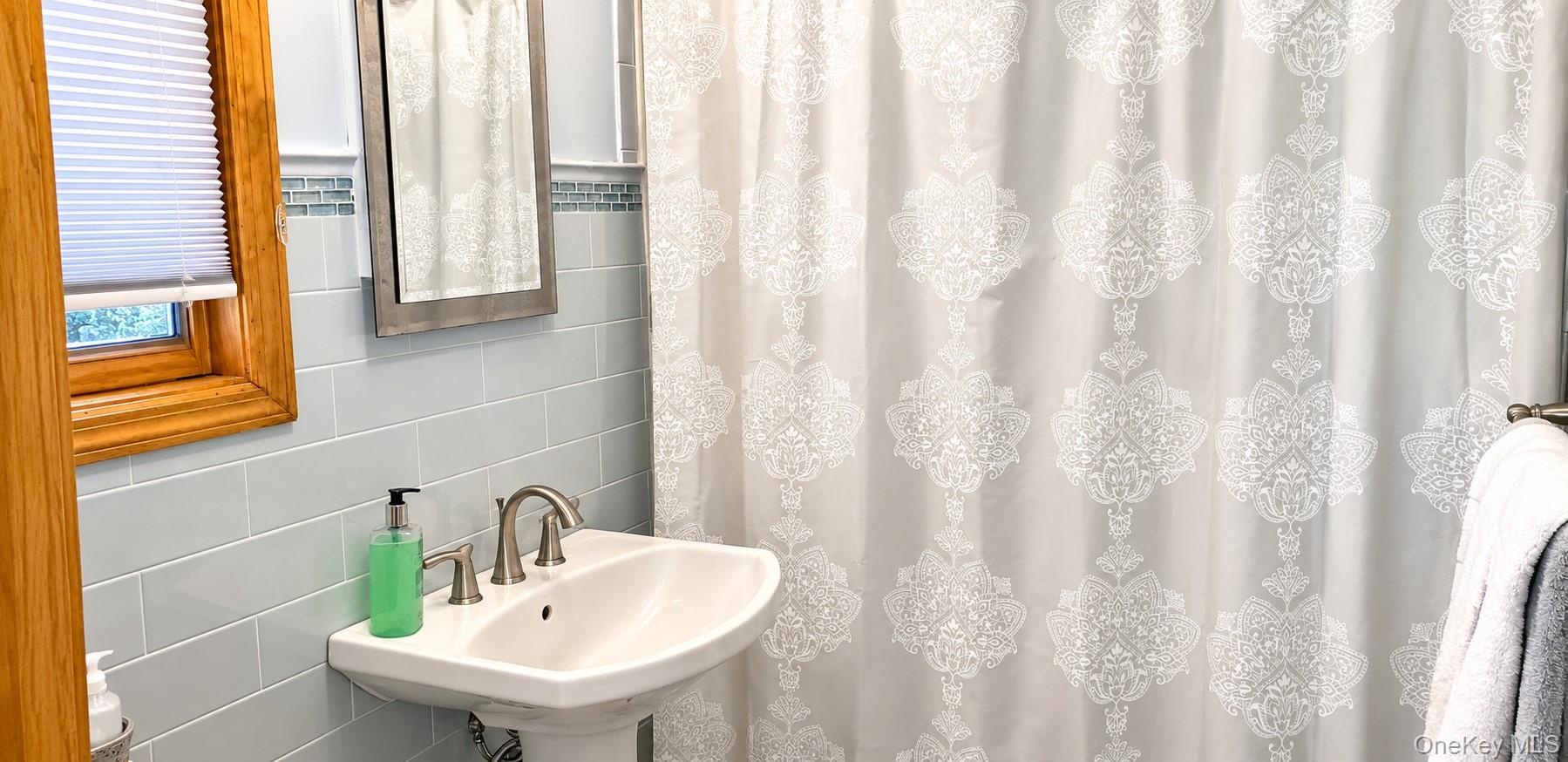 Wall-mounted pedestal sink with polished metal faucet, light blue subway tile backsplash, glass mosaic tile accent border, and natural wood-finish win