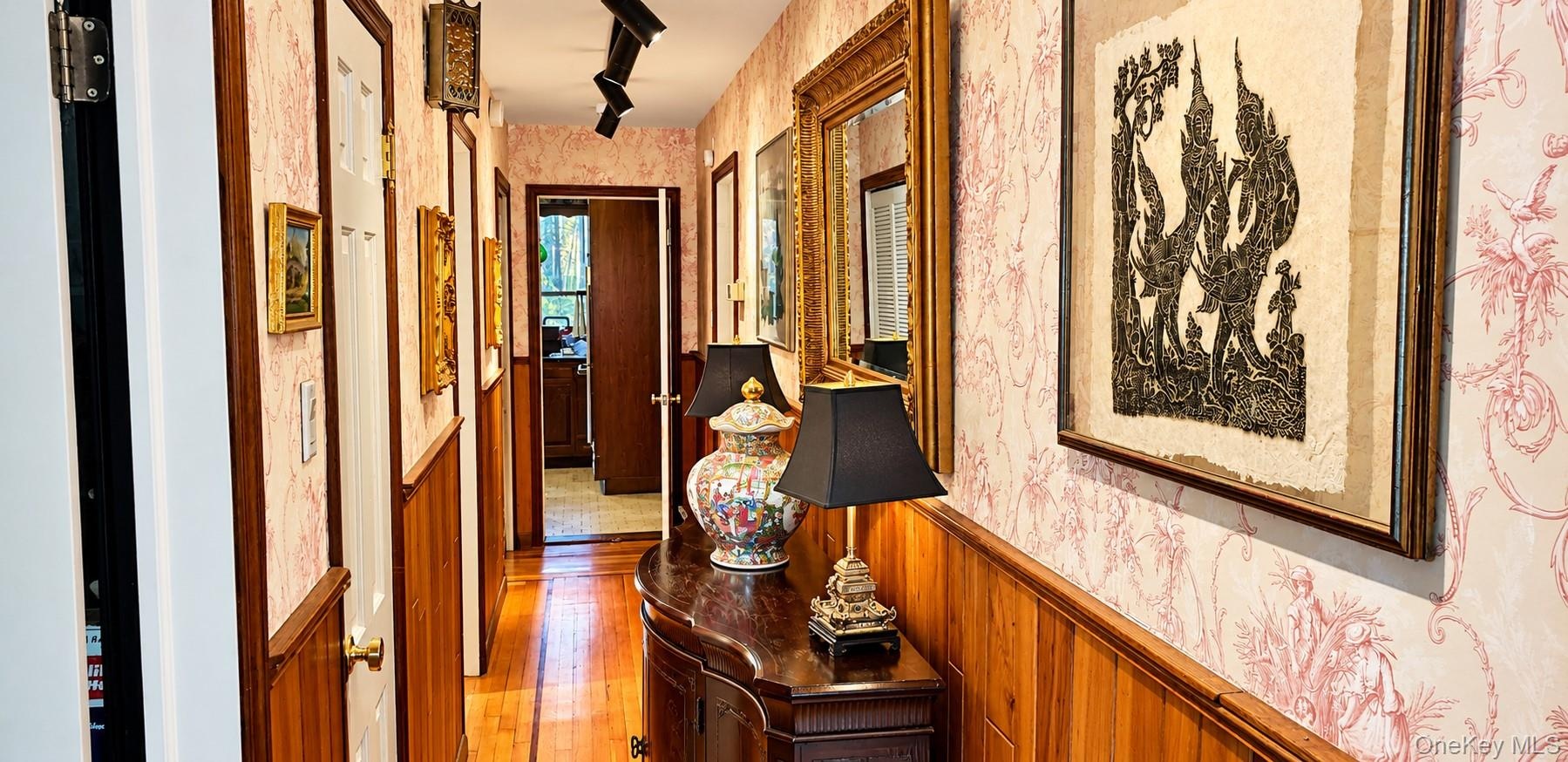 Hallway featuring patterned wallpaper, horizontal wood wainscoting, wood-finish flooring, and adjustable track lighting
