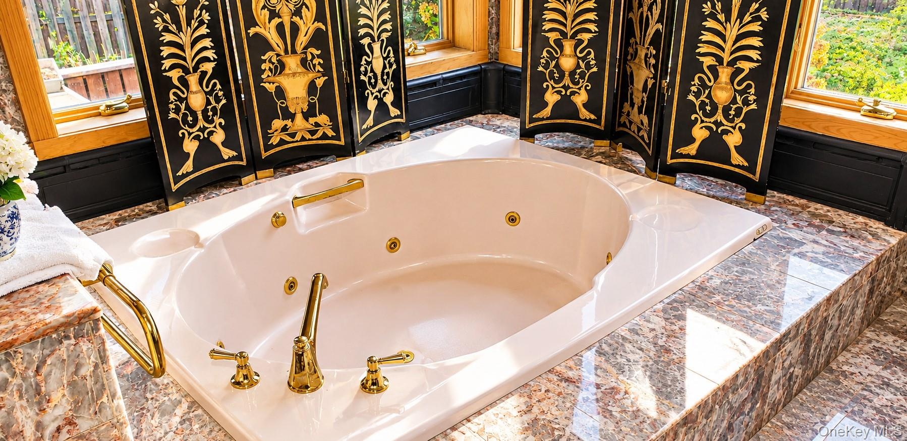 Jetted oval soaking tub featuring a natural stone surround, polished gold-tone hardware, and integrated gold-tone grab bars