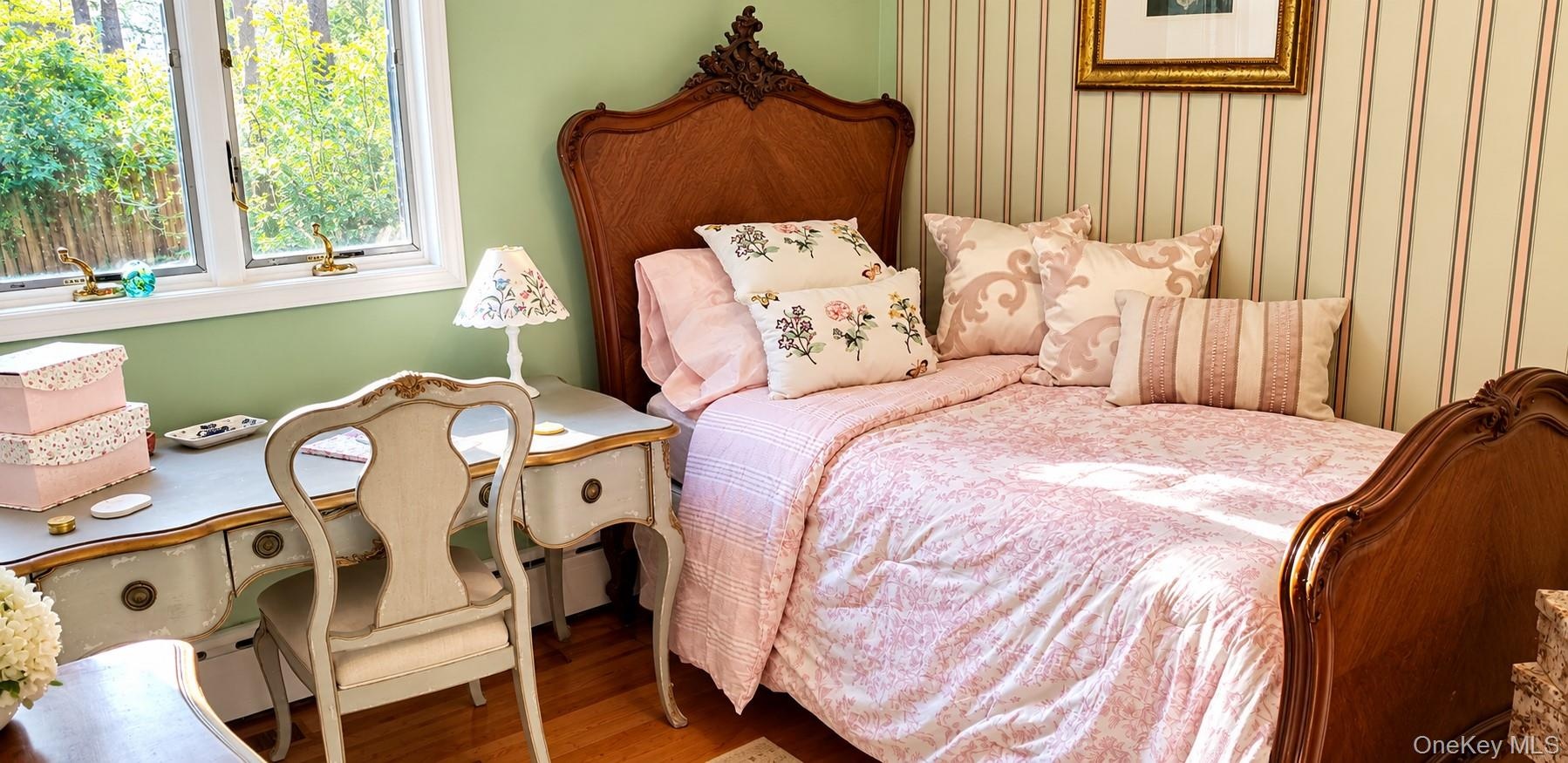 Bedroom featuring wood-finish flooring, multi-pane window, and vertical striped wallpaper accent wall