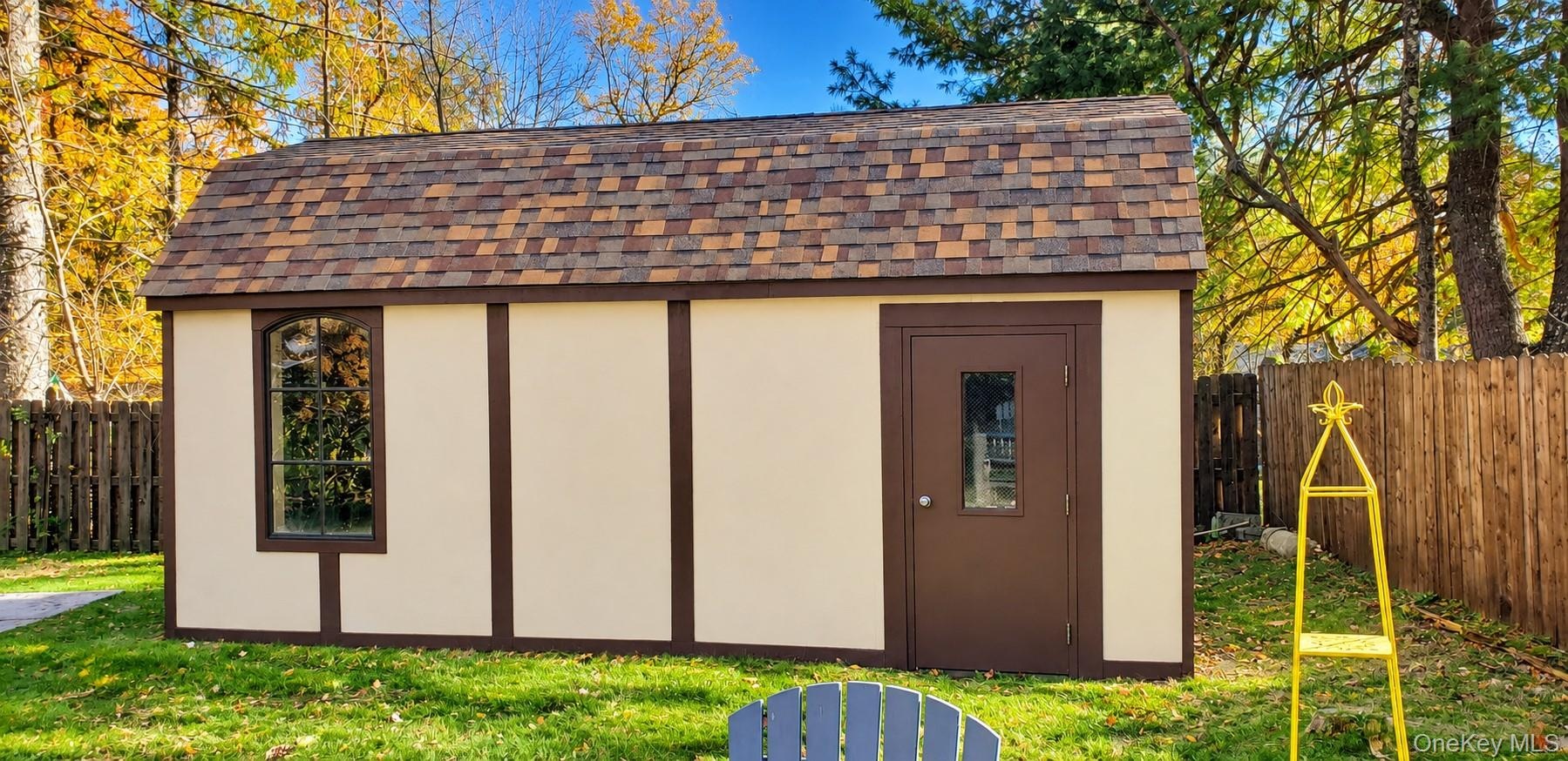 Exterior storage structure featuring asphalt shingle roofing, paneled siding, a single-entry door with a glass inset, and an arched window