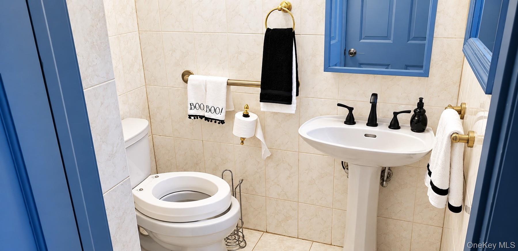 Bathroom featuring a white pedestal sink with a matte black widespread faucet, neutral-toned wall tile, a framed blue wall mirror, and brushed gold-to