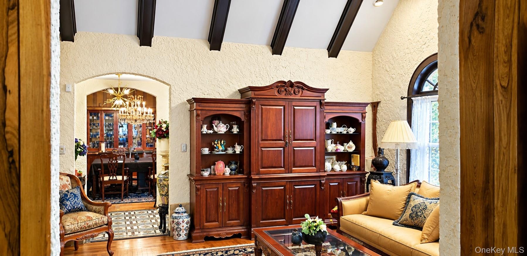 Vaulted ceiling featuring dark-stained exposed beams, arched entryway, and arched window with decorative molding