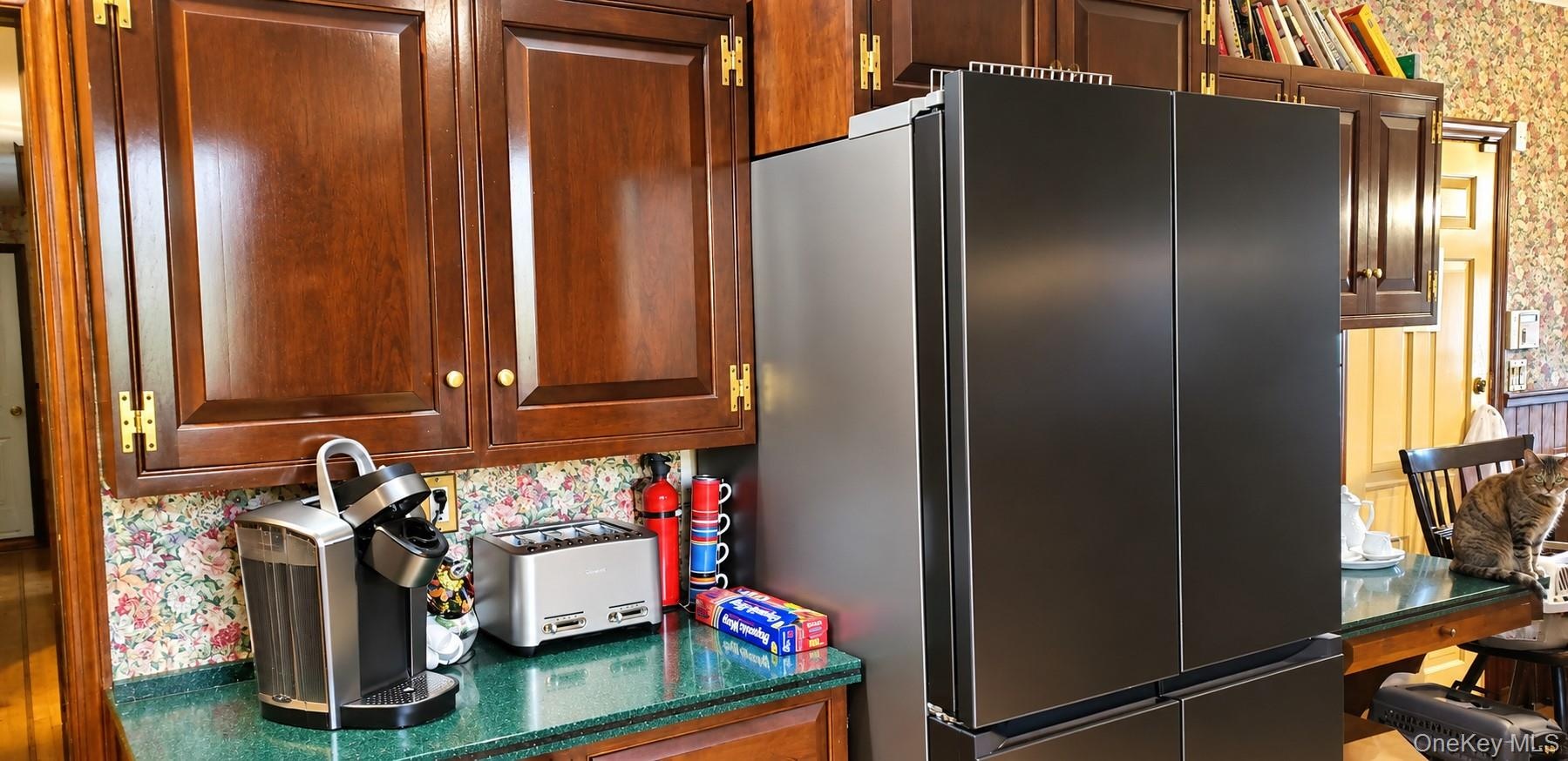 Dark wood cabinetry with exposed brass-tone hinges, green stone-finish countertop, and stainless steel French-door refrigerator