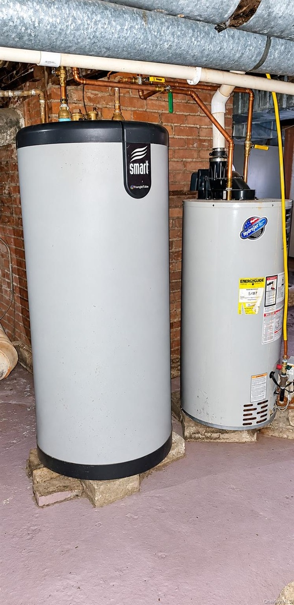 Mechanical system featuring an indirect-fired water heating tank and a separate vertical water heater with copper piping against a brick foundation wa
