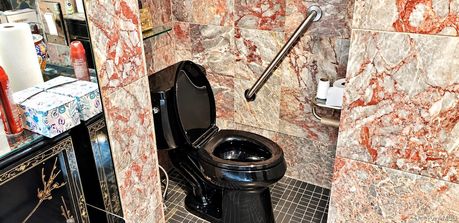 Bathroom featuring floor-to-ceiling multi-tonal red and grey stone tiling, black plumbing fixture, stainless steel wall-mounted grab bar, and dark-ton