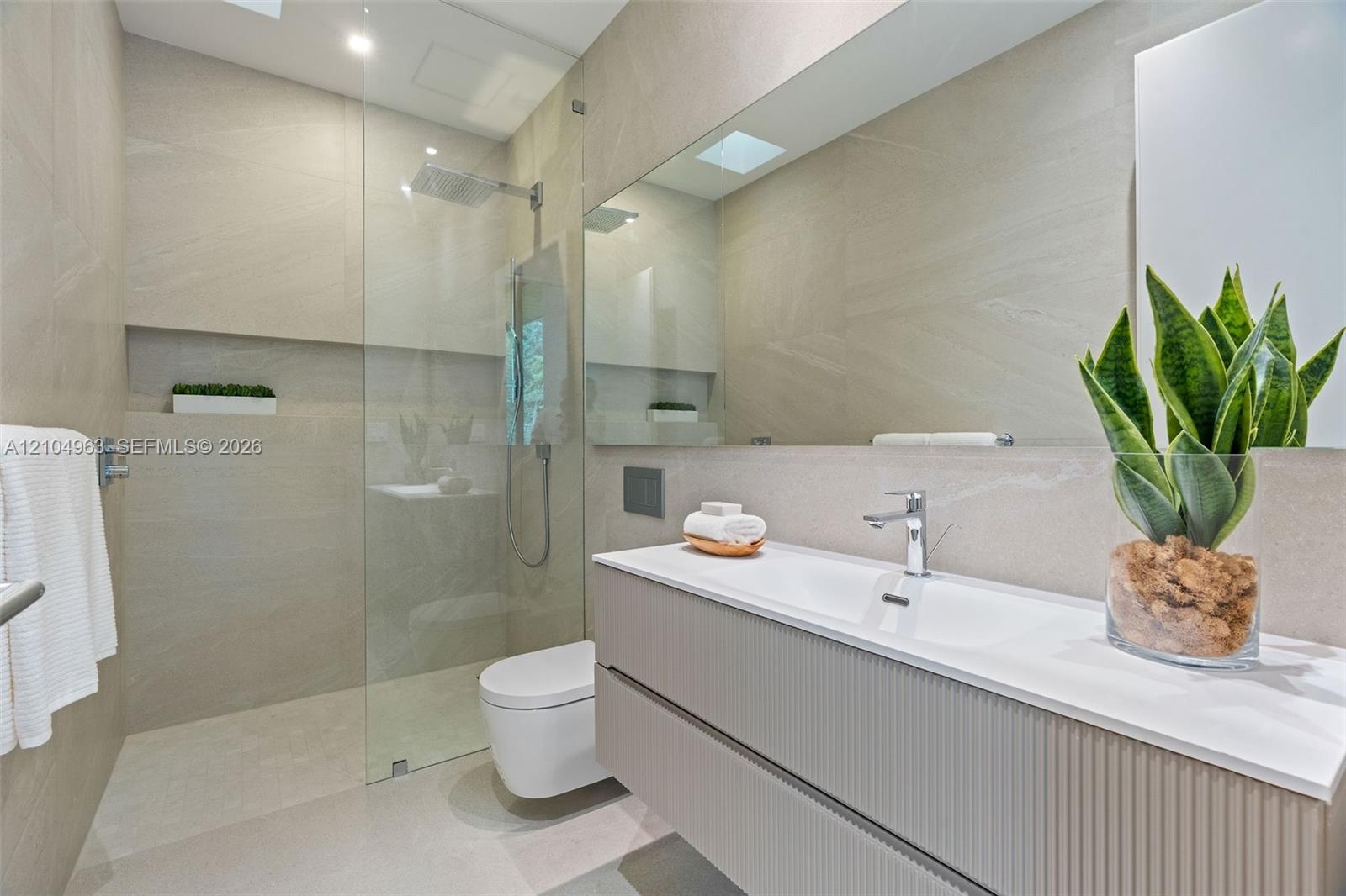 Modern bathroom featuring a textured floating vanity, integrated rectangular sink, wall-to-wall mirror, glass-enclosed walk-in shower with a rain-styl
