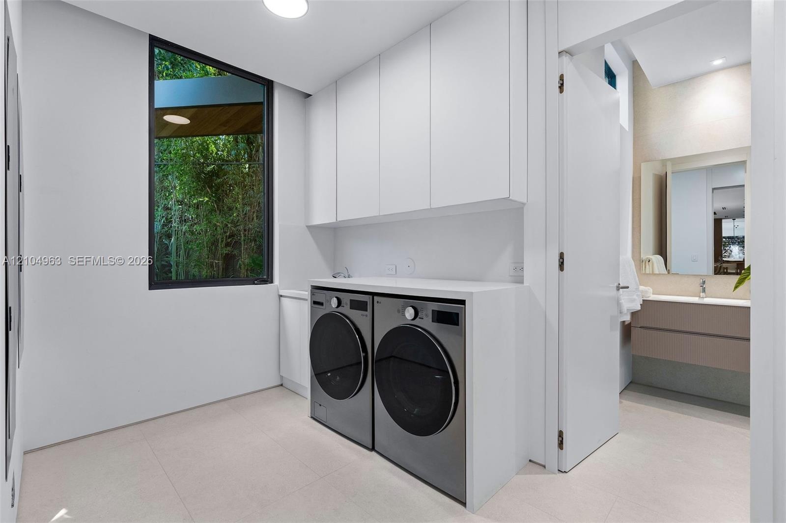 Laundry room featuring floor-to-ceiling cabinetry, custom solid-surface countertops, large-format tile flooring, and a window with natural foliage exp