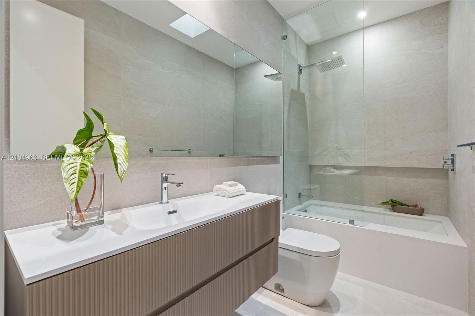 Floating vanity featuring a ribbed textured finish, integrated white basin, wall-to-wall mirror, glass-enclosed shower and tub combination, and full-h