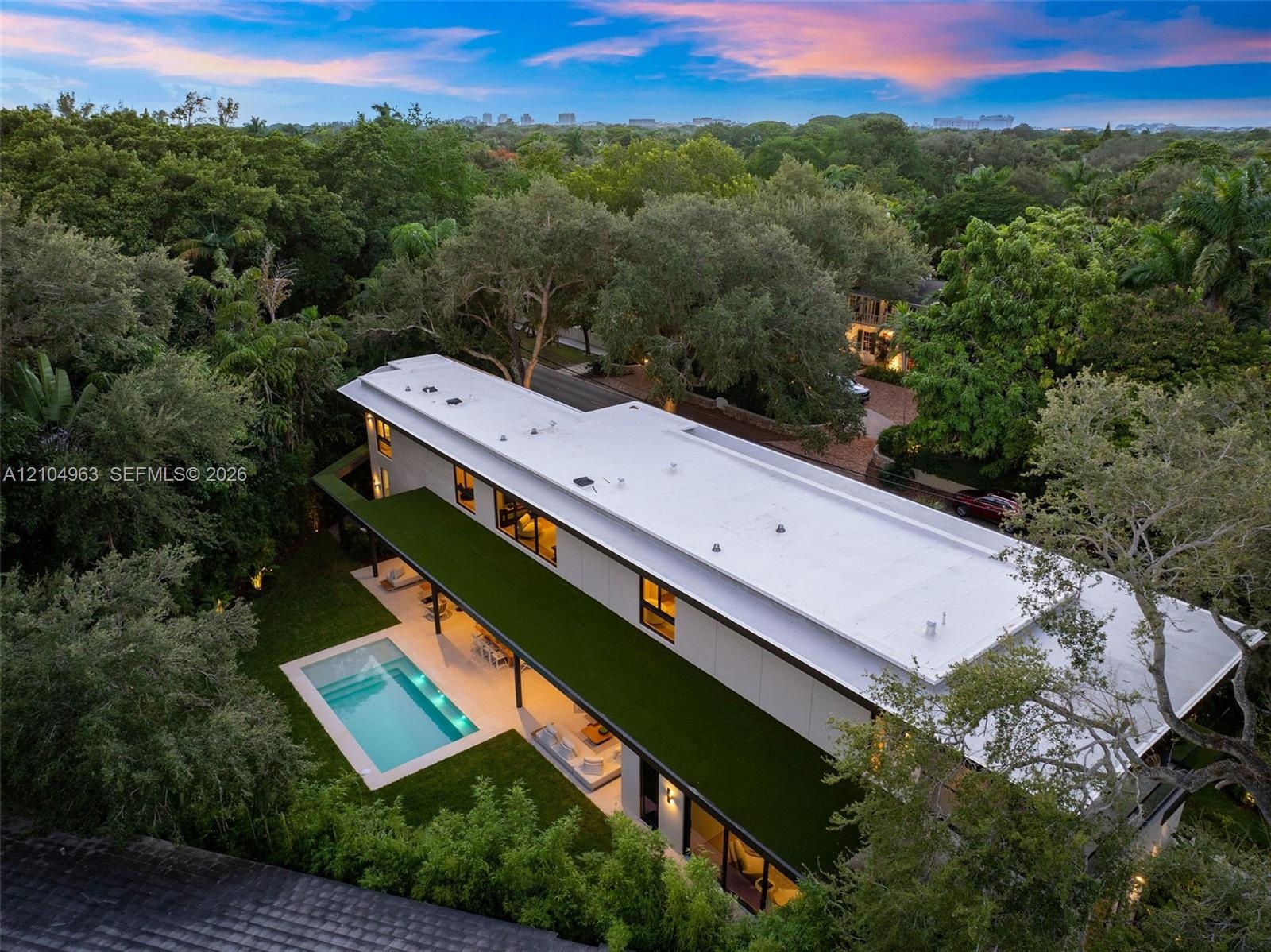 Modern two-story structure featuring a flat roofline, minimalist facade, in-ground swimming pool, expansive hardscaped patio, and mature perimeter lan