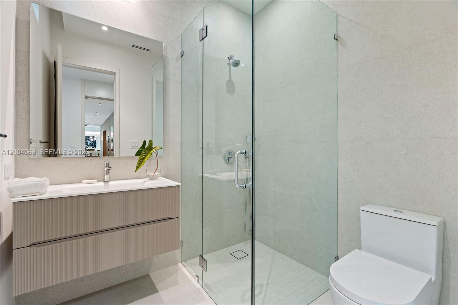 Floating vanity with integrated sink, walk-in shower featuring frameless glass enclosure, polished chrome hardware, and large-format wall tiling