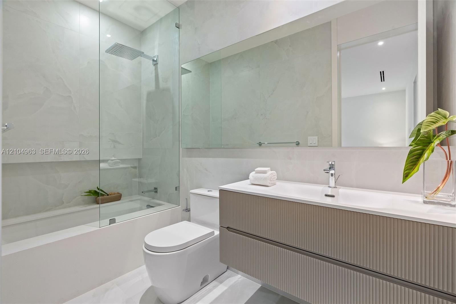 Floating vanity with ribbed cabinetry and integrated sink, frameless glass shower enclosure, rainfall showerhead, large wall-spanning mirror, and neut