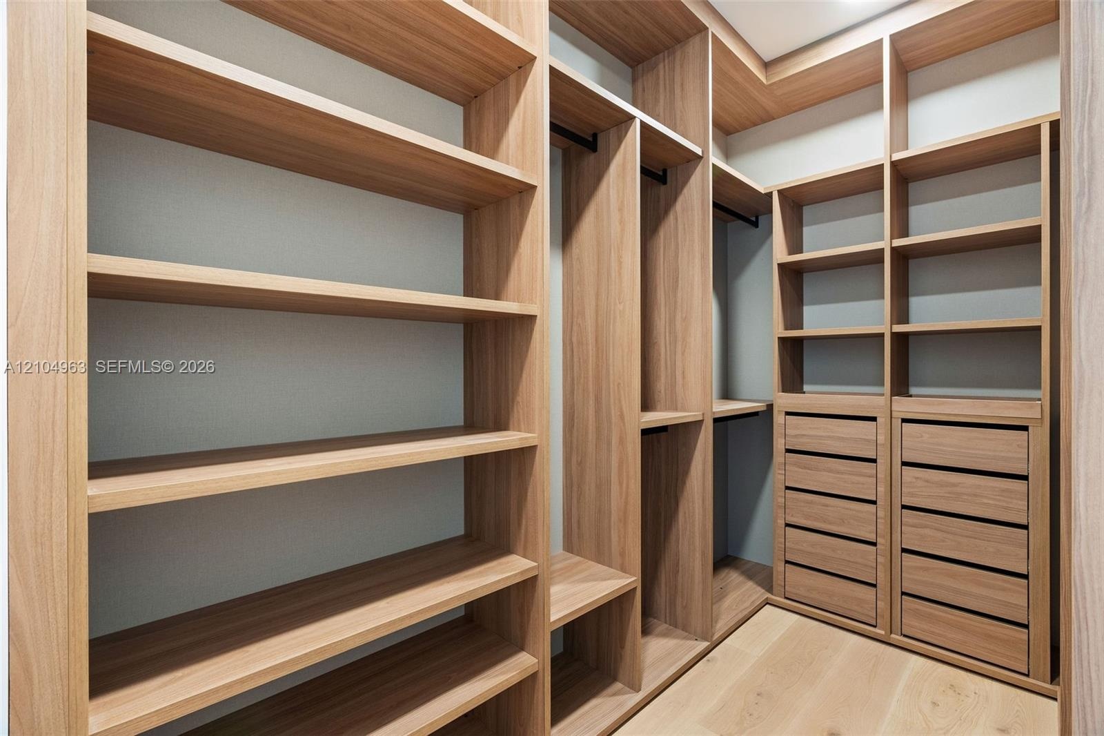 Custom walk-in closet featuring built-in wood-finish shelving, integrated hanging rods, and multi-drawer cabinetry with wood-finish flooring