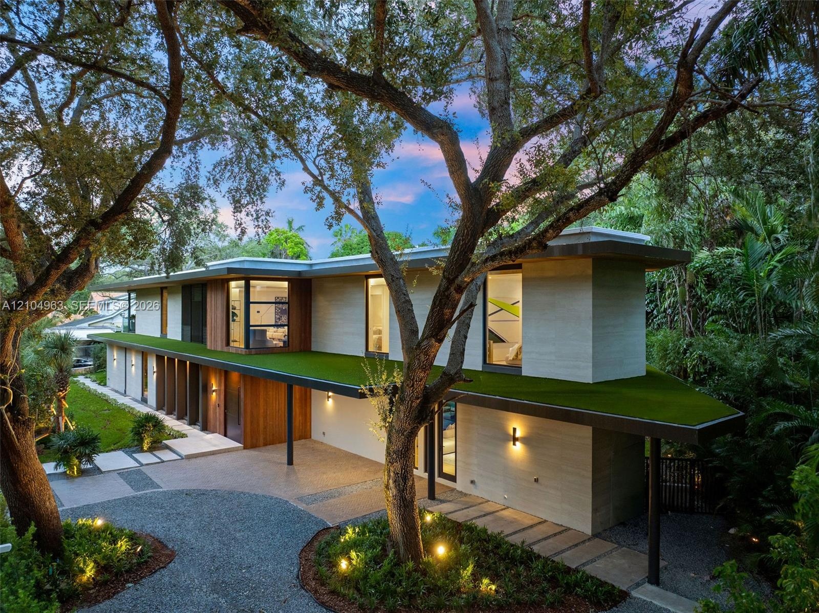 Modern architectural exterior featuring a flat roofline, horizontal stone and wood siding, integrated green roof canopy, gravel motor court, and linea