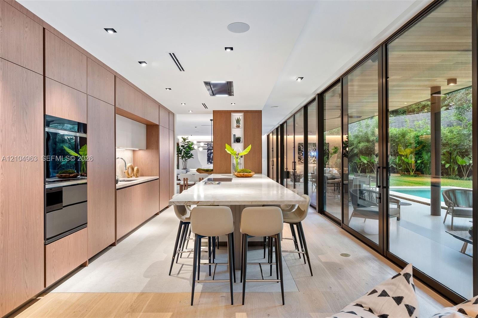 Kitchen featuring floor-to-ceiling wood-finish cabinetry, central island with stone countertop, recessed lighting, and full-length glass sliding doors