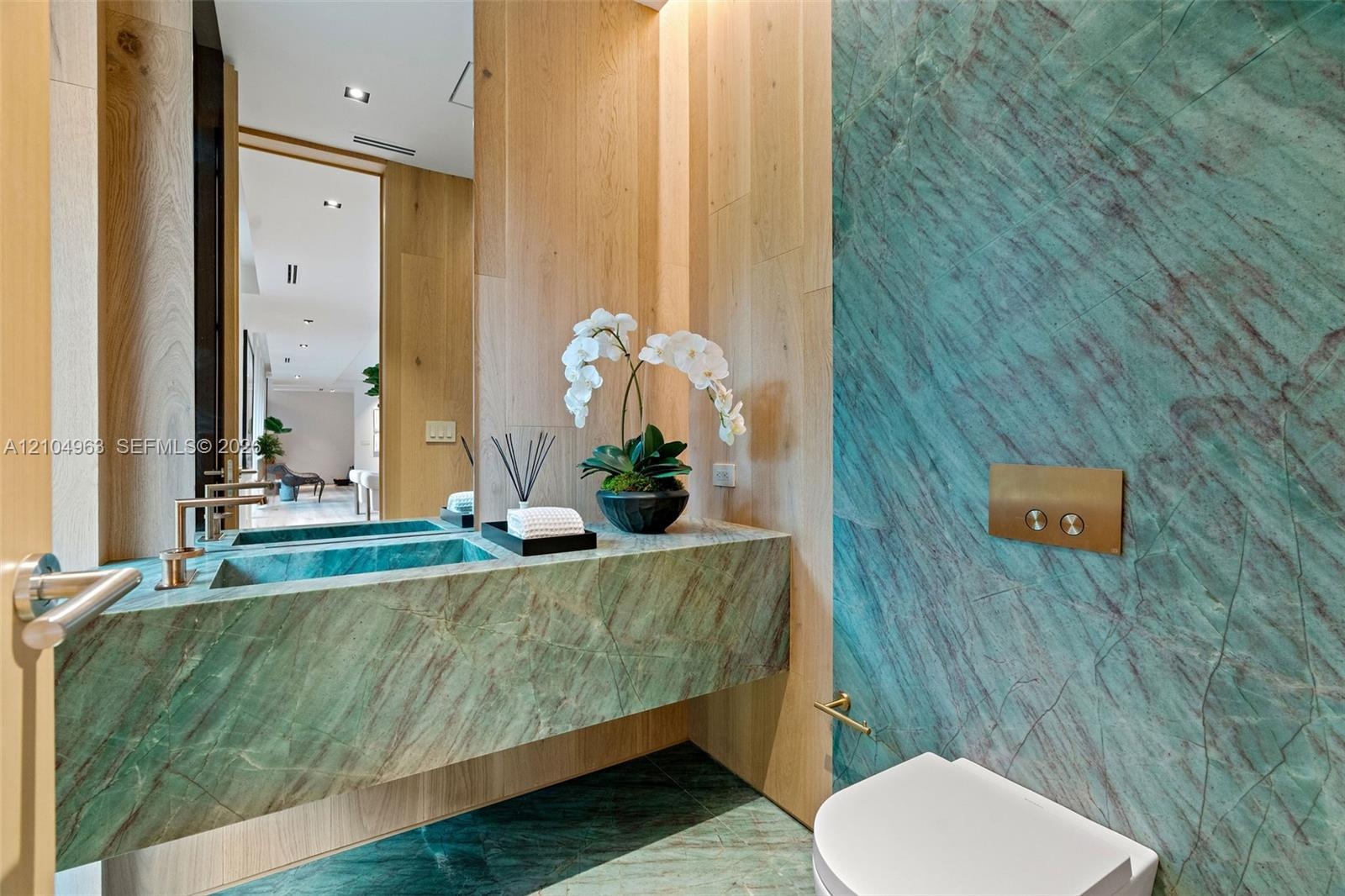 Floating vanity with integrated basin, teal stone wall cladding, floor-to-ceiling wood paneling, wall-mounted metallic flush actuator, and recessed ce